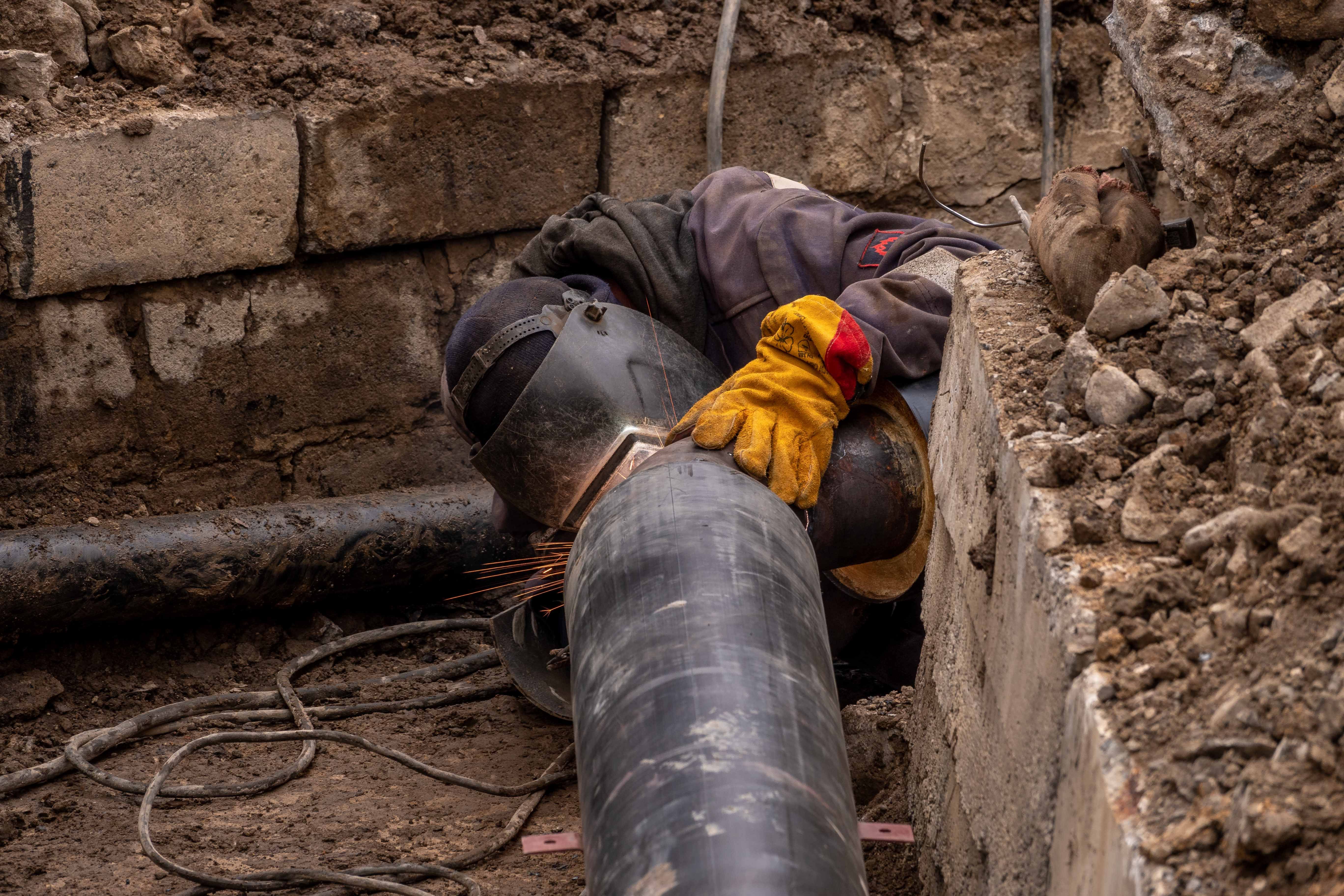 Welder in a trench joining a large-diameter steel pipeline
